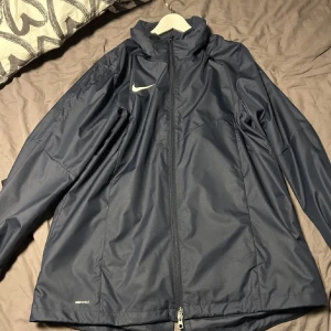Nike vindjacka - Helt ny vindjacka från Nike säljes pga att den är för stor. Sitter som L. Luvan sitter under ett kardborreband som man kan se på bilden. Hör av dig vid intresse eller fler frågor😊