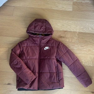 Nike Puffer - Vin/mörkröd Puffer från Nike. Näst intill oanvänd så skicket är väldigt bra. Storlek L ( Damstorlek ) så är du kille med strl. S/M  så borde den passa. 