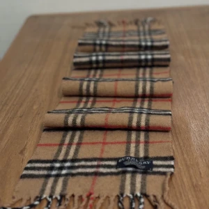 Burberry halsduk - Burberry halsduk i den klassiska färgen, 100% lammull. Perfekt till vinter. Bra skick inga hål osv. Nypris 4600, mitt pris 800kr. Bara att skriva vid frågor eller funderingar och lägg ett bud