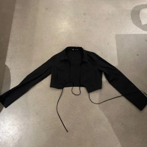 Svart skjortblus med knytdetalj på bröstet. - Svart skjorta/top/blus med knytdetalj på bröstet. Använd 1 gång, storlek M.  Relativt liten i storlek så funkar även för S.
