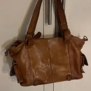 En snygg brun skinnväska från secondhandbutik. Den är i bra skick!☺️ Längd: 32 cm Höjd: 24 cm