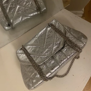 Silvrig väska  - Iiten silvrig väska med två stycken fack inuti. Rymmer allt man behöver ha med sig! Använd ett fåtal gånger så inga större defekter förutom att kedjan missfärgats en aning! 