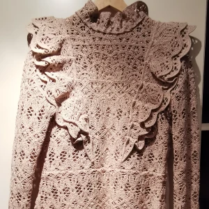 Virkad topp med volang - Långärmad virkad topp utan foder med knäppning i ryggen och med hög hals. Volang både fram och bak, över axlarna. Nypris ca 600 kr. P/N 09044112. 55% bomull, 39% polyamid, 6% polyester. Strl S. 