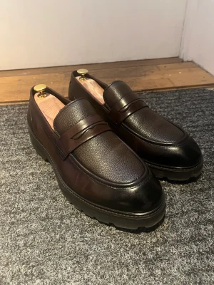 Loafers från TGA by Ahler - Helt nya loafers i storlek 43/44 från anrika företaget TGA by Ahler.  Använda 1-2 gånger. Nypris 1700kr, mitt pris 900kr (köpare betalar för frakt) Låda samt andra accessoarer tillkommer dock tillkommer INTE skosträckaren!