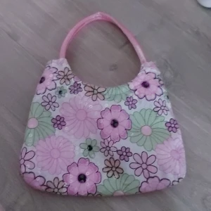 Blomig väska - Blommig väska som är vit ,grön och rosa med Blommor. Använd 1-3 gånger och har ingen skråma.
