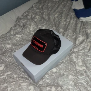 John hatter keps - Rödsvart keps från märket John hatter & Co, metallbrickan är lite skrapad och kepsen är pyttelite solblekt.