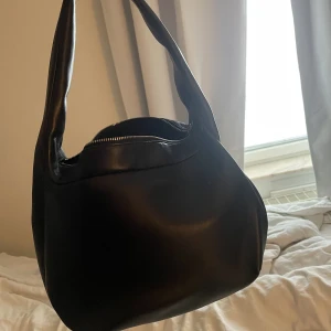 COS läderväska - Väska från cos, modell leather mini Shoulder bag nypris 1150 kr, använd fåtal gånger, väldigt rymlig med en liten innerficka. Mått: 24x23.5