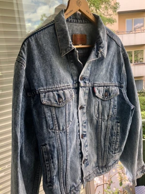 Vintage Levis Jeansjacka från 80 talet - Fräsch Levis  jeansjacka , äkta 80 tal, tillverkad i Italien. Storlek large. Stor i storleken. Ärmlängd ca 60 cm. Hals  ca 47 cm.  Längd ca 63 cm Bredd ca 52 Acid Wash , stentvättad. Mycket bra skick.
