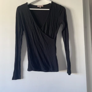 Svart topp med korsad tyg - En svart enkel långärmad topp med korsat tyg över bysten vilken gör en snygg urringning! 158-164 (eller s)