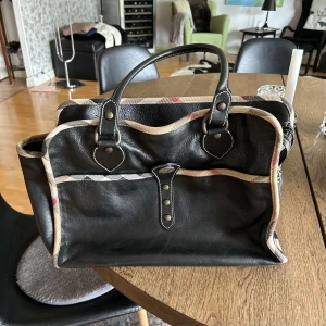 Burberry väska vintage - Säljer en äkta Burberry väska i riktigt skinn. Väskan är rejäl och tung, måtten är 38x15x26cm. Absolut felfri, utan skavanker och skador. Hel och ren, i toppskick!  Säljes för 10.000:-, svarar inte på skambud. Fler bilder finns vid serilst intresse.