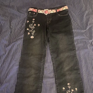 Svarta jeans med blom detaljer - Riktigt fina med blommor på och ett rosa skärp med ett hjärta. Det går att ta av skärpet.