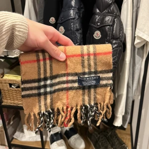 Burberry halsduk  - Burberry halsduk i den klassiska färgen, 100% lammull. Bra skick inga hål osv. En lite mindre modell ca 100cm lång, vanliga modellen är ca 150cm lång. Nypris 4600, mitt pris 900kr. Bara att skriva vid frågor eller funderingar! :)