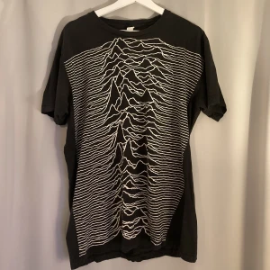 Joy Division T-Shirt - En T-shirt med ett all over print från ”Unknown Pleasures” av Joy Division. Storlek large, men passar mer som en lång medium. Tröjan är köpt begagnad, men väldigt lätt använt av mig själv.