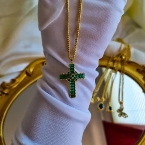 Emerald cross necklace  - Unisex, helt nytt och oanvänt. MATERIAL Hänge: Zirkon, Mässing, 18k guldpläterad Kedja: 18k guldpläterad, rostfritt stål HÄNGE STORLEK 27 mm bred, 38 mm lång, 5,5 mm tjock. LÄNGD; 18 TUM. KADMIUMFRI OCH BLYFRI KVALITETER.  VATTENTÅLIG SLÄCKFRITT HÅLLAS LÄ