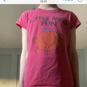 En röd T-shirt - En röd T-shirt med ett liten glatt ansikte på och en text ovanför ”little miss fun”