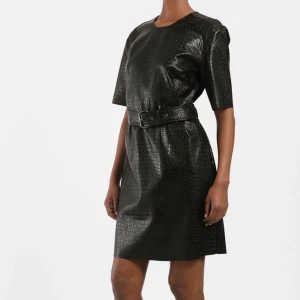 Svart klänning- Twist & Tango strl 36 - Svart läcker klänning från Twist ang Tango. Storlek: 36  Svart läder klänning med rund hals i präglat krokomönster.  Den har en metalldragkedja baktill, korta ärmar och ett metallspänne i midjan.  Bältet är avtagbart för en rak passform. (Klänningen är gjord av veganskt läder)  Aldrig använd + prislappen sitter kvar.