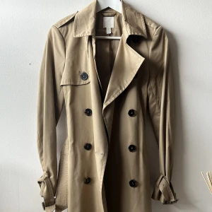 Trenchcoat - Säljer denna beiga trenchcoaten från H&M jag köpte för många år sedan. Har dock aldrig använt den då den är en storlek för liten för mig (storlek 34).