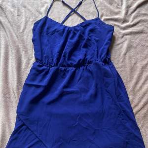 En kort blå klänning med kors i ryggen och omlott