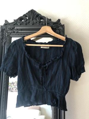 Blå-svart somrig blus - Superfin blå-svart blus med rosett från Urban outfitters! Den är superskön och fin men blivit för liten för mig! Använt få gånger!  Kan mötas upp i Lund eller Malmö beroende på tid!