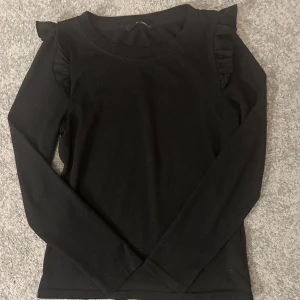 Långärmad topp med volang  - Svart långärmad tröja med volangdetalj på axlarna. Endast använd ett fåtal gånger. 