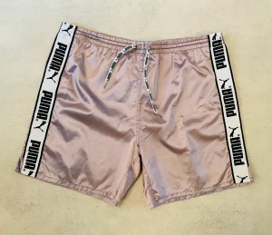 Rosa vintage Puma shorts stl. L - Vintage glansiga Puma shorts från 90-talet i bra skick! Ovanlig färg på dessa klassiska shorts! 