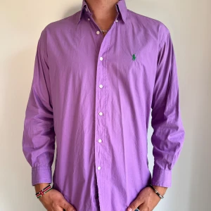 Ralph Lauren skjorta  - Lila Ralph Lauren skjorta med armlängd 32/33 och kragstorlek 14.5. Skjortan är i bra skick men är lite blekt längst ner på ärmen (se bild). Modellen är 186 cm lång. Orginalpris ca 1500 kr och nu endast 499. 