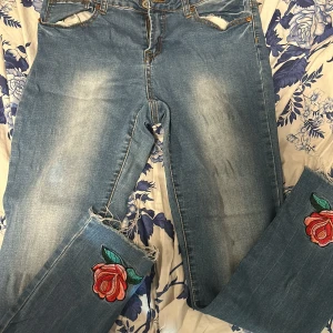 Blå jeans med blomma - Blå jeans med blomma. De är i använt skick och en hålla på byxan har gått sönder. De är i ungefärlig storlek L/XL
