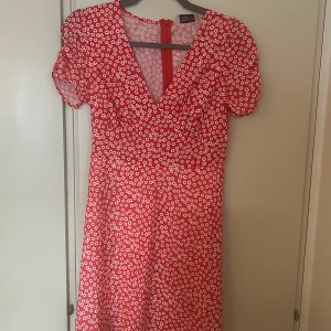 Blommig klänning - En röd- och vitblommig sommarklänning som är helt oanvänd. Är väldigt tunn i materialet och går lite över knäna.
