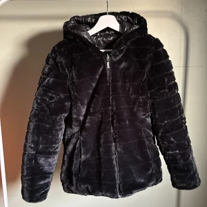 Vändbar fluffig jacks - Svart jacka i storlek M 40-42. Med mjuk fluffig fejkpäls. Vändbar med fickor på utsidan åt båda håll som jackan vänds. I nyskick, använd endast en gång. 