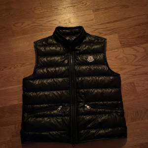 Moncler gui väst - Hej! Säljer min Moncler Gui väst i färgen svart. Inga defekter, alltså ser den i princip helt ny ut! Du kan självklart betala med plick för ett säkert köp!
