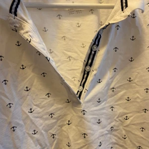 T-shirt med knappar  -  En modern twist på den klassiska t-shirten. Stilren och bekväm, perfekt för en avslappnad. Bära några gånger 