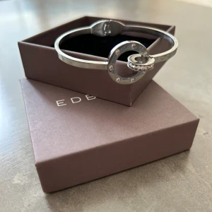 Ida Bangle Steel armband Edblad - Silvrigt armband från Edblad. Storlek Small, använt ca 2 gånger. Detaljer hämtade från deras hemsida: Diameter stor ring 20 mm, liten ring 12 mm, storlek skena 3x2 mm Innerstorlek 16 cm. Kubisk zirkon, blankt rostfritt stål även nickelsäkert. 