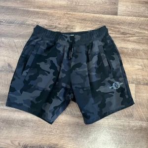 Better Bodies shorts, storlek M - Better Bodies helt nya shorts. Shorts i kamouflage-mönster med en liten logotyp på vänster ben. Shortsen har en resår i midjan och en dragsko för att justera passformen. Det finns två fickor på sidorna och en ficka med dragkedja på baksidan.