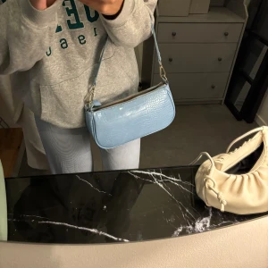 Blå väska  - Säljer denna snygga väskan pga garderobsrensning, aldrig använd därav bandet och påsen i väskan, köpt för 700kr säljer nu för 250