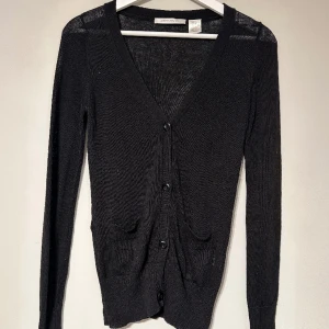 Svart kofta - En tunt stickad svart kofta från côté femme. Koftan är lång och v-ringad, med två framfickor. 