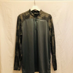 Träningströja halfzip från Craft - Behaglig träningströja med luft återcirkulerande material. Nyskick, inga defekter. Militärgrön & grå. Finns även i svart & grå.