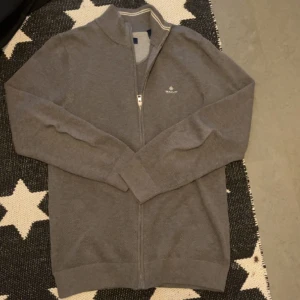 Stickad Gant helzip - En grå snygg stickad helzip från Gant. Är i toppskick och har ej använts myckrt eftersom den är för stor för mig. Storlek M men sitter nästan som L. Nypris är 1600 kr , mitt pris är 600.