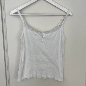 Brandy Melville vitt linne spets - Gulligt vitt linne med knappar och spets från Brandy Melville. Onesize (men ca S). Tunna axelband. Fint skick. 100% bomull.