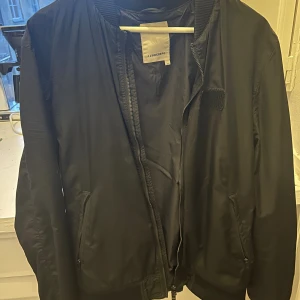 Svart Bomberjacka J.Lindeberg  - Säljer en tunn bomberjacka från J.Linderberg. En perfekt övergångsjacka som passar till både vår, sommar och höst. Nypris runt 2000 kr. Måttligt använd och inga fläckar. 