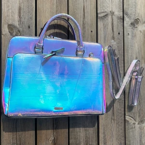 Skinnydip holographic laptopväska - Holographic laptop väska från Skinnydip med axelband, köpt ifrån London men aldrig använd.  Ficka på baksidan med magnetlås, ytterfack med 5 fickor. Stort fack för laptop och en innerficka.  CA; 34 cm lång, 27 cm hög, 5 cm bred (7 cm med ytterfacket)