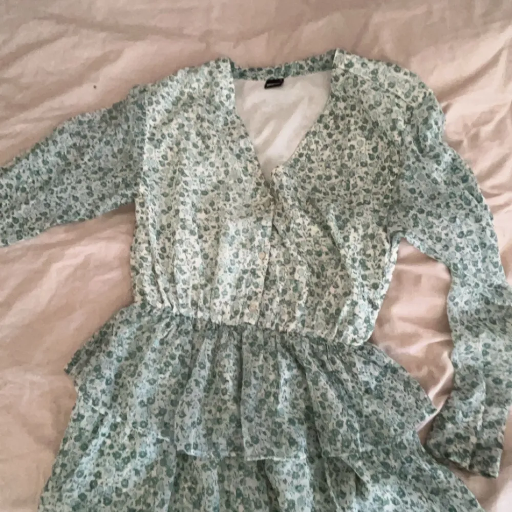 Jag använde den som skolavslutnings klänning och den är använd väldigt sparsamt, Max tre gånger. Den är svagt vit, med blågröna blommor på med volangkjol tillhörande💗💗. Klänningar.