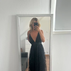 Balklänning - Superfin balklänning i nyskick som aldrig använts. Svart med ett glittrigt paljettmönster. Går att justera banden i ryggen och därför lätt att anpassa. Köpt för 1800kr