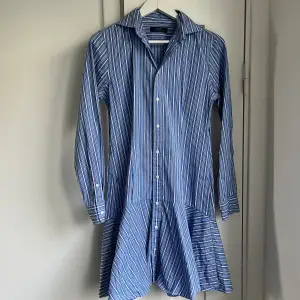 Polo Ralph Lauren figursydd Skjortklänning vitblå-randig. Perfekt skick, som oanvänd. ”Kjolen” går asymmetriskt, längre i bak och kortare i fram.