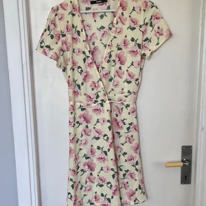 Sommarklänning  - En kort gul sommarklänning med rosa blommor från bik bok. Oanvänd.