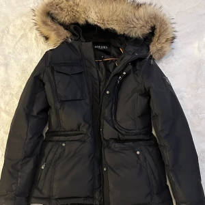 Hollies jacka stl 38 - Hollies vinterjacka, använd 2 säsonger. Justerbar midja, mycket bra skick. Äkta päls. Obs! Jackan sitter som 36