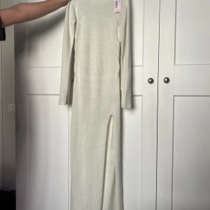 Lång klänning  - Vit ish färgad klänning, glittrig. Tajt passform, men stretchigt material. Helt oanvänd med lappen kvar. Slits på vänstra benet och på båda ärmarna.
