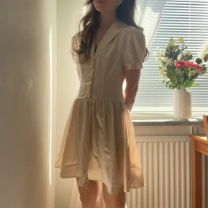 Champagne-färgad klänning i satin - Finaste klänningen i satin och har en fantastiskt fin passform och faller fint.  Små söta puffärmar och guldiga knappar. Helt ny!  Storlek XS