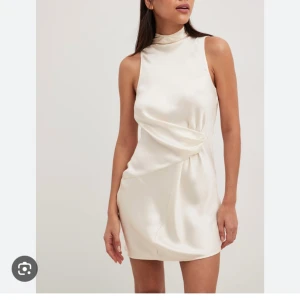 Vit satin klänning - Vit klänning i satin från NAKD med öppen rygg samt knytning i ryggen. I oanvänt skick med lappen kvar då den va lite kort på mig (178 cm lång). I storlek 42 men passar även 40. Slutsåld på NAKDs hemsida. 