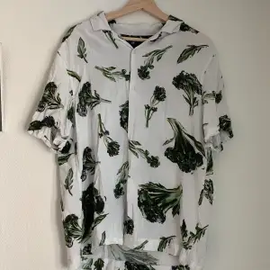 En fin vit skjorta med växter. Skjortan är i bra skick men den är lagad på baksidan, se sista bilden. Det förstör inte dess helthetsintryck och går bra att använda ändå!