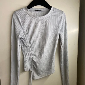 Asymmetrisk Ljusblå Ribbad tröja st XS - Säljer en ljusblå tröja i storlek XS. Den är ribbad och har snören som man kan dra ihop tröjan med. 